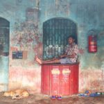An old postoffice in which a man is sitting on a big letter box and a dog is sleeping on the floor