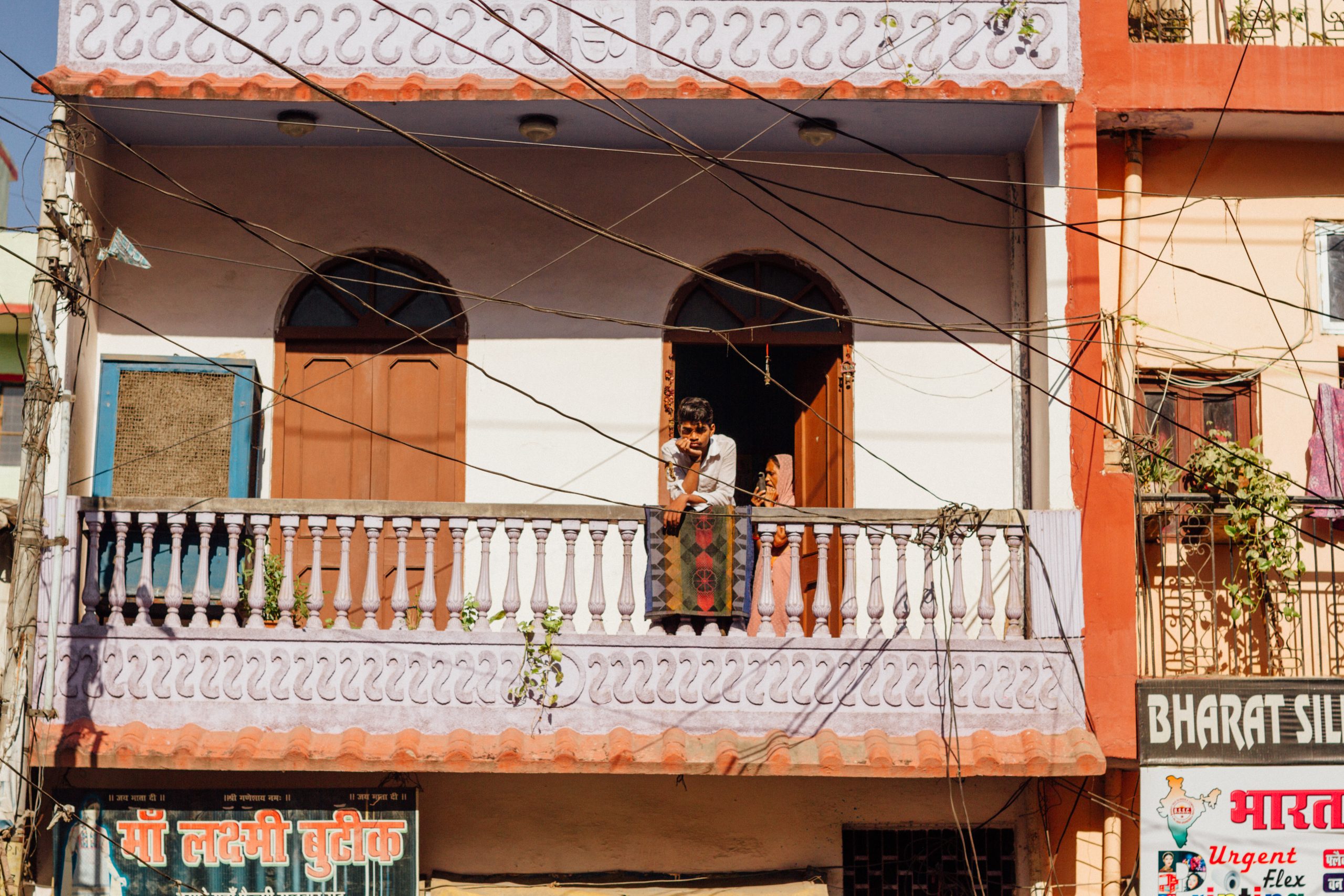boy looking out from balcony with two arched doors behind him leaning on a railing