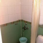 faucet pouring into blue bucket behind a shower curtain that is pulled back